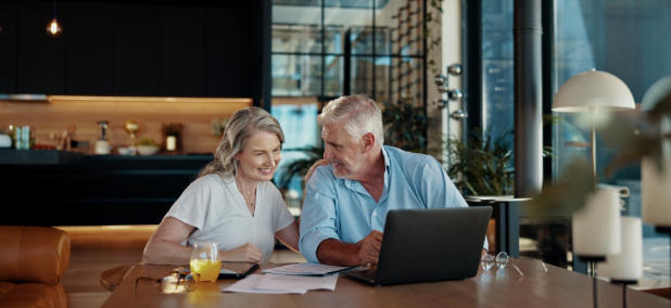Smiling senior couple reviewing retirement income documents together at home using a laptop